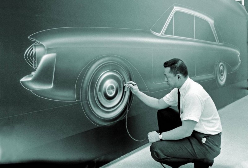 Larry Shinoda, designer of the 1963 C2 Corvette Sting Ray, crouching and editing a design of a car on the wall before him